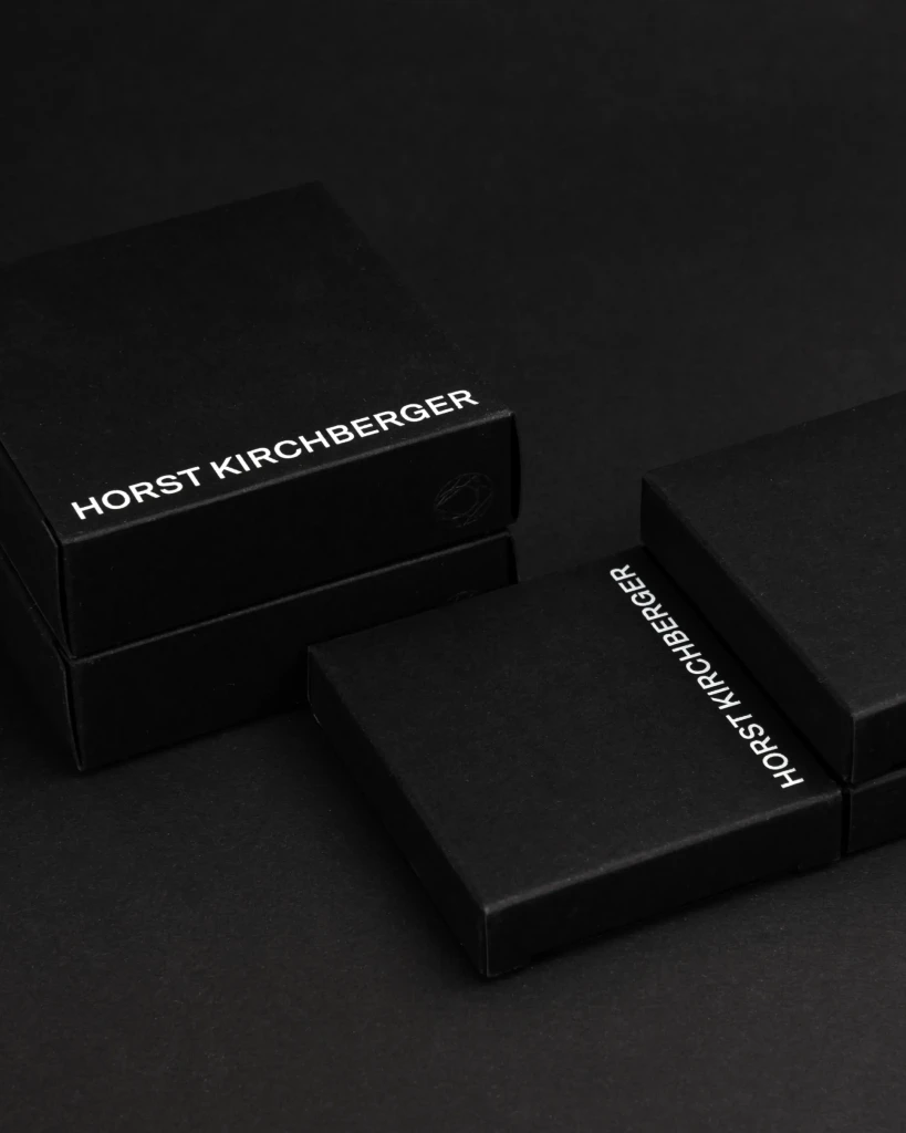 schwarze Kosmetik Karton-Schachteln mit dem Horst Kirchberger Logo liegen ordenlich auf einem schwarzen Hintergrund