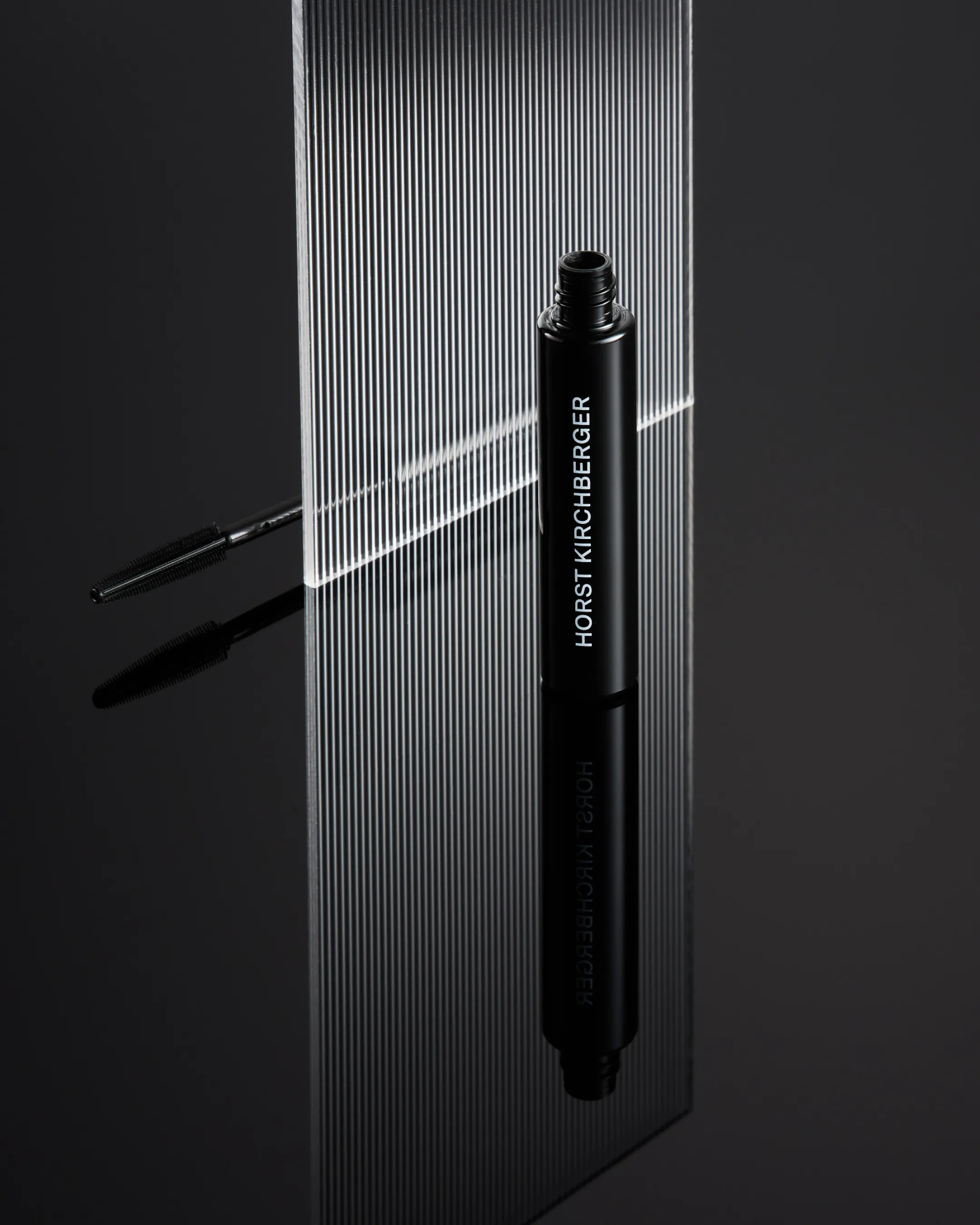 Geöffnete schwarze Mascara von Horst Kirchberger, stehend auf einer reflektierenden schwarzen Fläche.