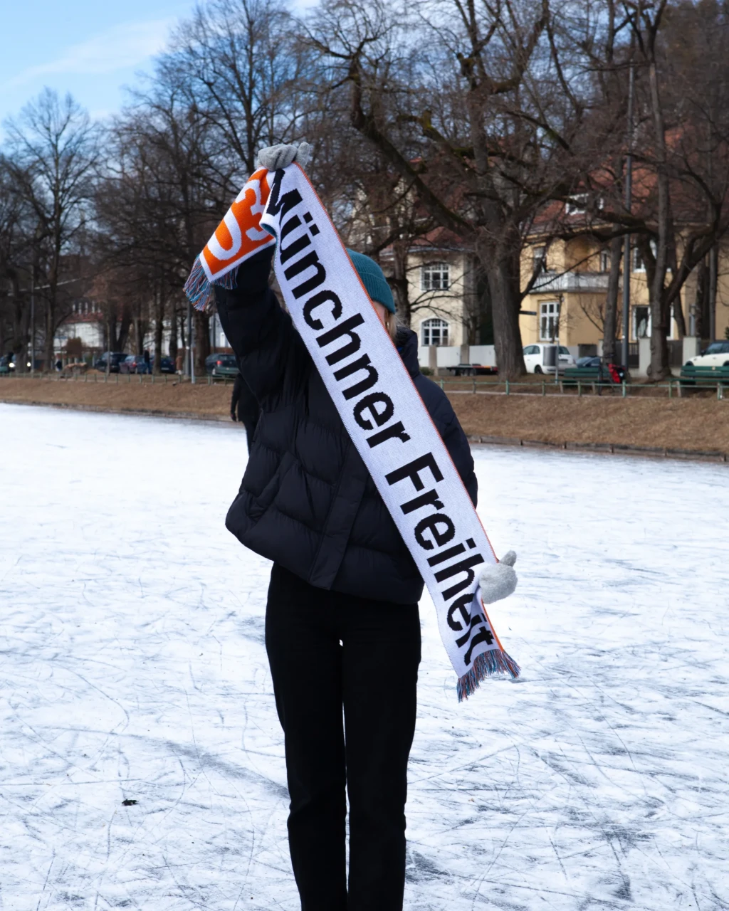 Fußballlschal, wird von Person auf gefrorenem Kanal hochgehalten. In U-Bahn Design der Schriftzug "U3 Münchener Freiheit"