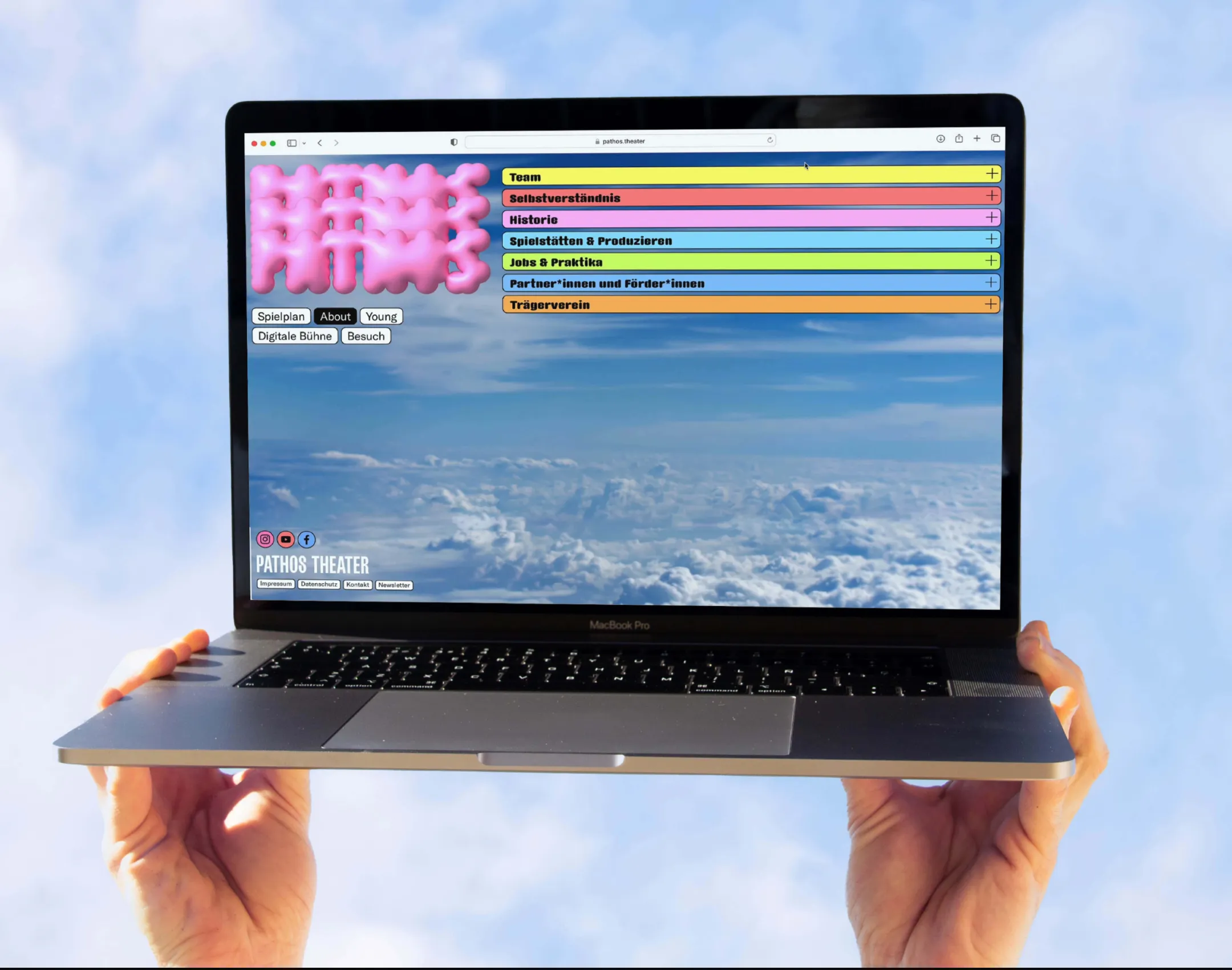 Die Startseite der Pathos Website auf einem Laptop, der von zwei Händen in den Himmel gehalten wird
