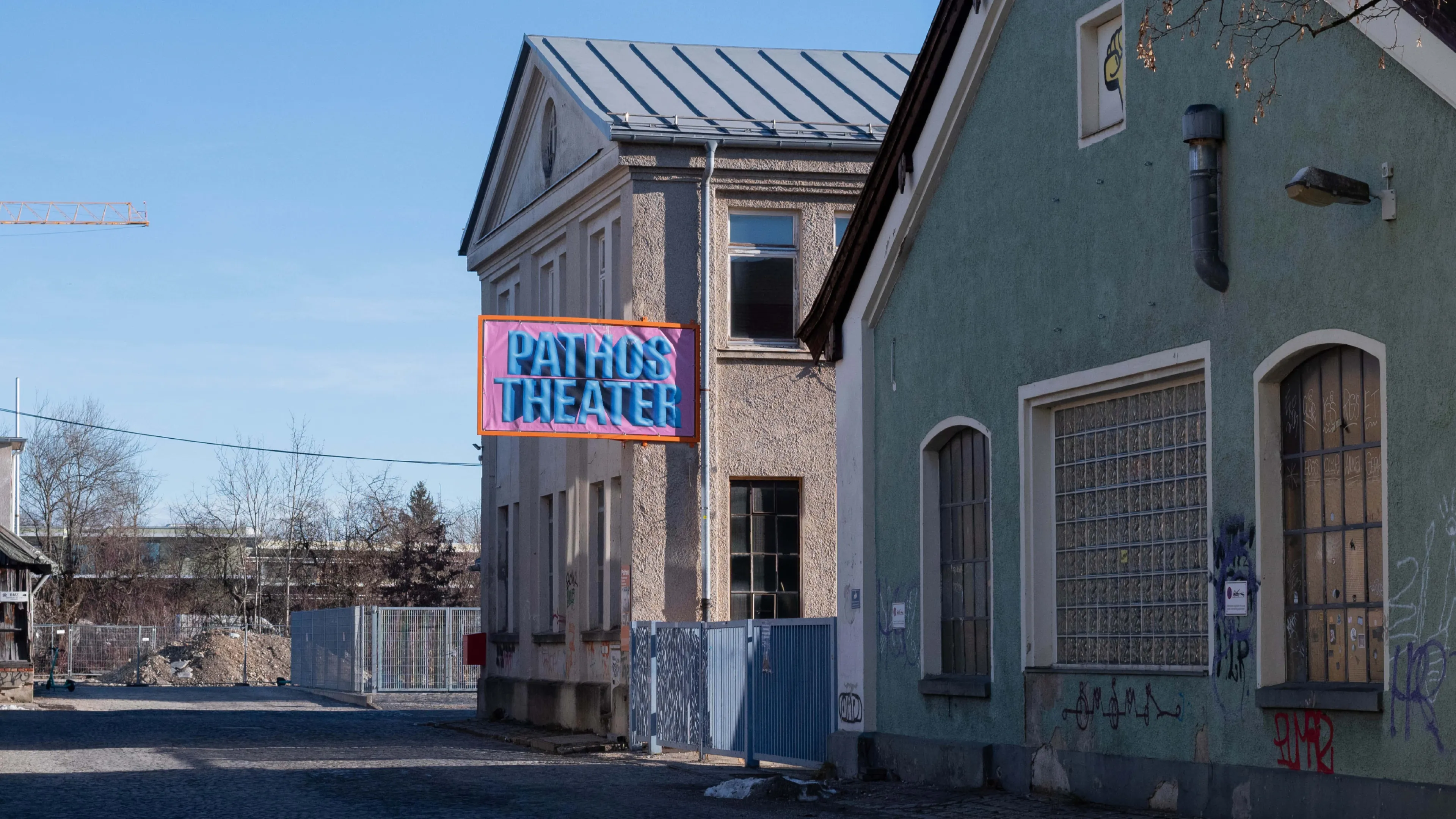 Außengelände des Pathos Theaters mit Gebäudebschilderung mit blauem Bubble-Type Schriftzug auf pinkem Hintergrund