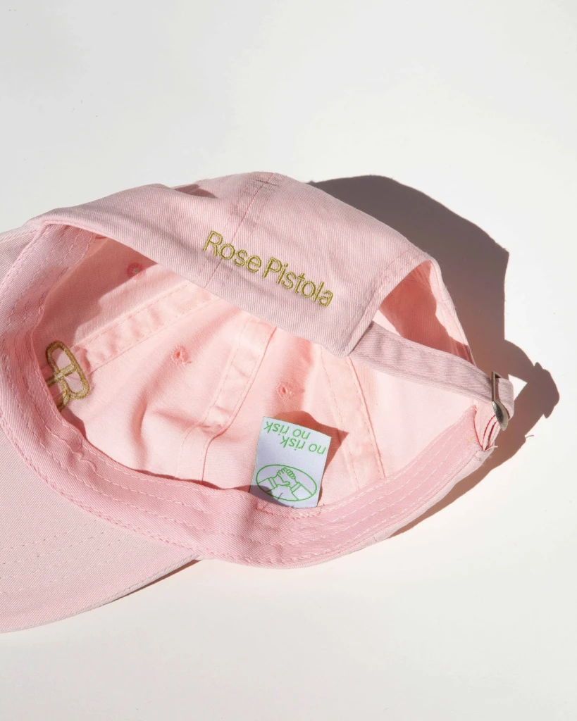 Detailaufnahme der rosa Merch Cap mit gold besticktem Rose Pistola Logo vor weißem Hintergrund